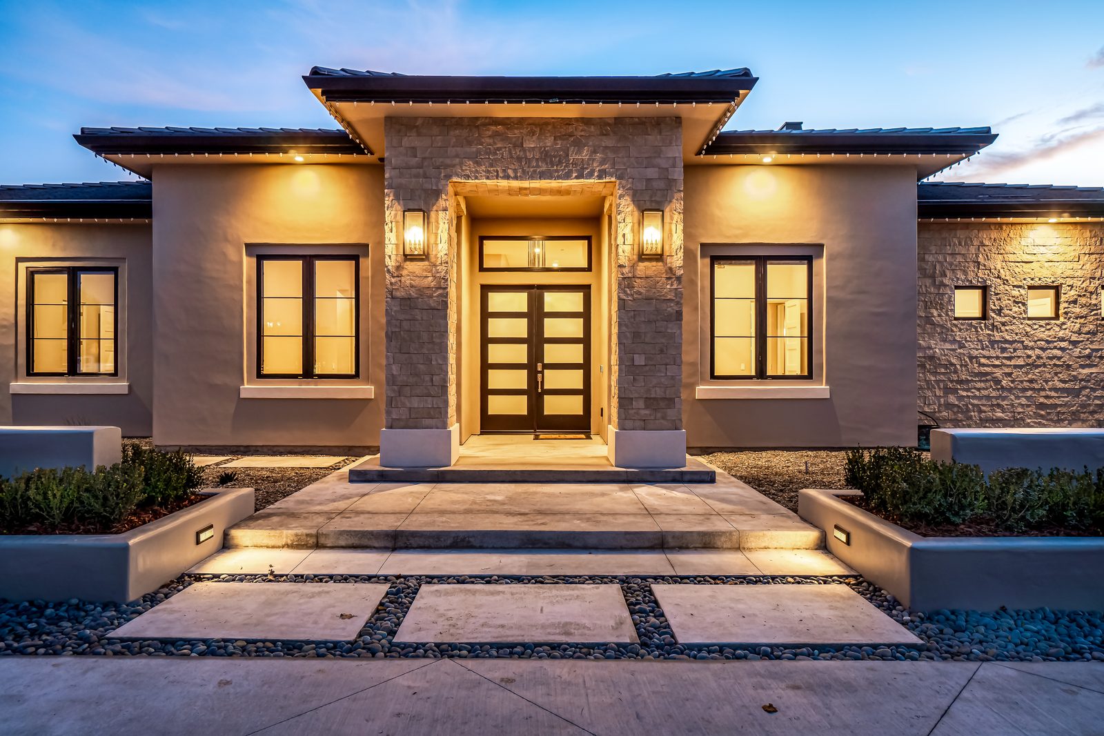 Stone-clad front entry with glass-panel double doors and lantern sconces at dusk, Templeton