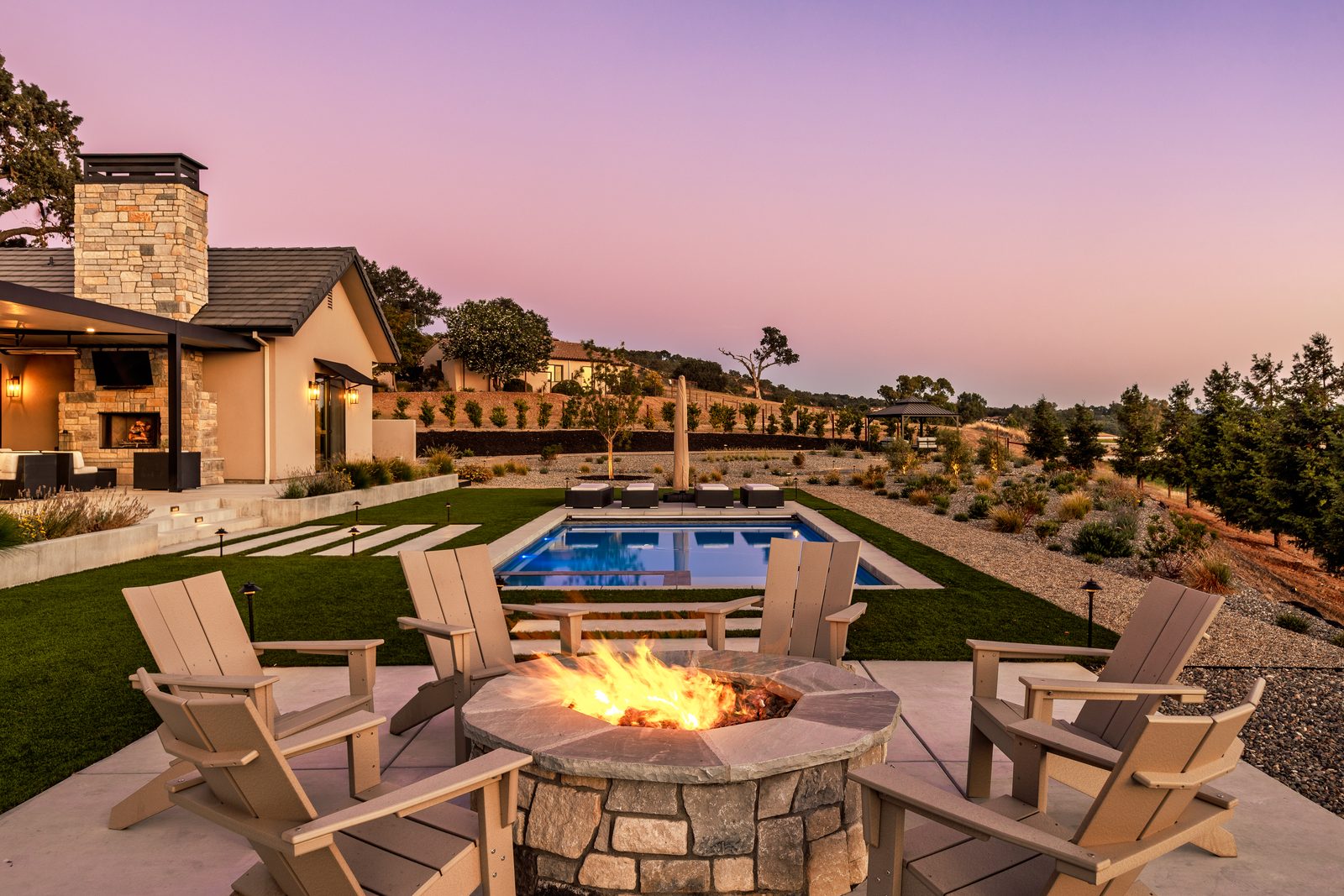 Stone fire pit with lounge chairs above the pool at sunset, Templeton