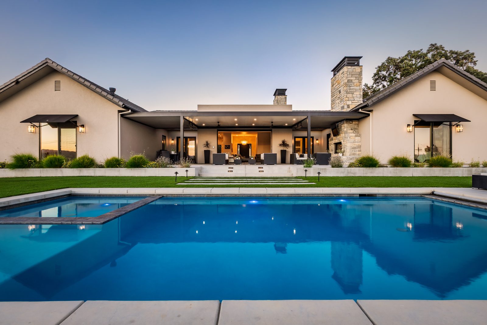 Pool and spa in front of the covered patios and stone chimney of a single-story ranch home, Templeton