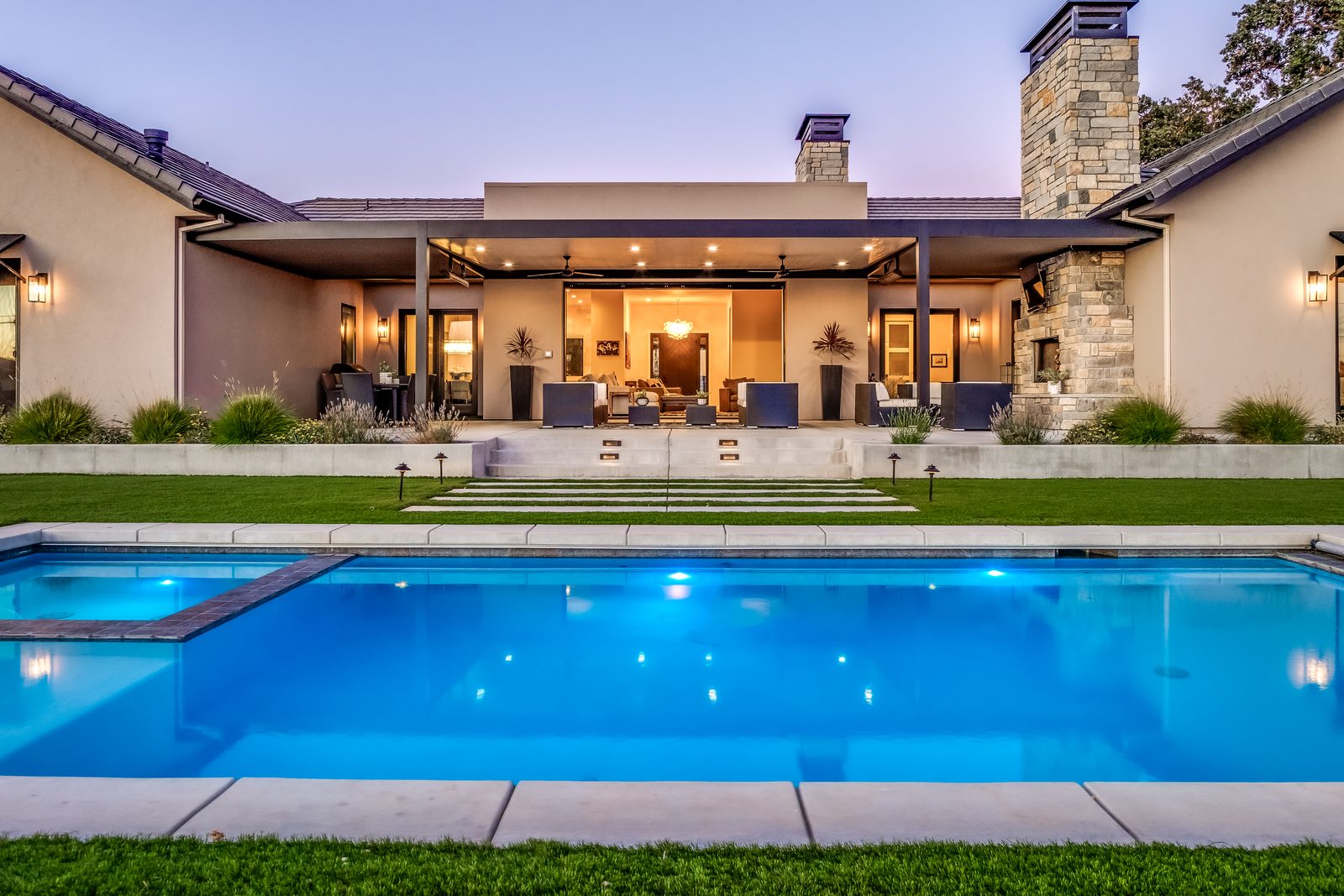 Single-story Modern Ranch home at dusk with a lit pool, stone chimney and open covered patio, Templeton