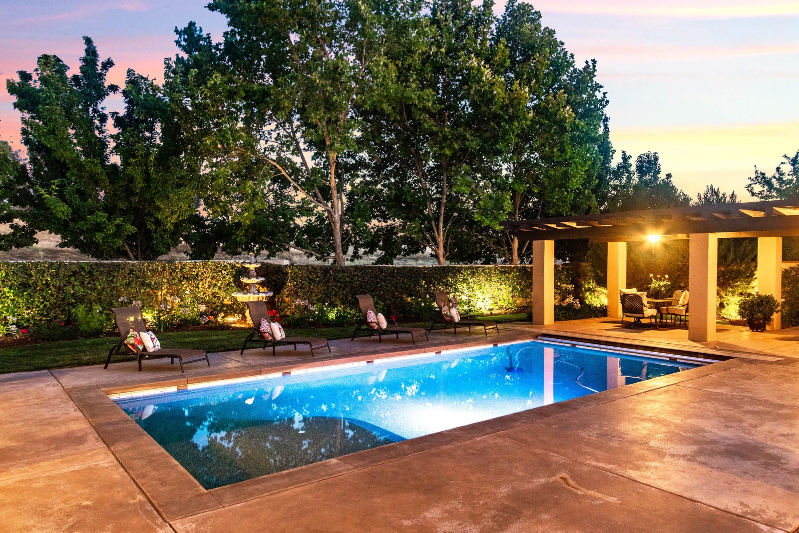 Lit pool and covered pergola seating at dusk in a hedged backyard, Tuscan Revival home in Paso Robles
